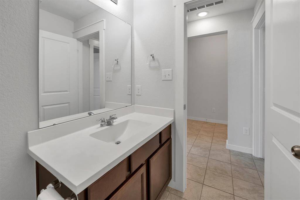 This photo shows a modern bathroom with a sleek white countertop, under-mounted sink, and large mirror. The room features neutral tile flooring and walls, providing a clean and spacious feel.