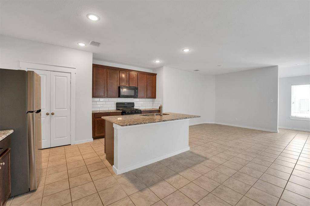 This spacious kitchen features modern stainless steel appliances, a central island with granite countertops, and ample cabinet space. It opens into a bright, tiled living area, perfect for entertaining.