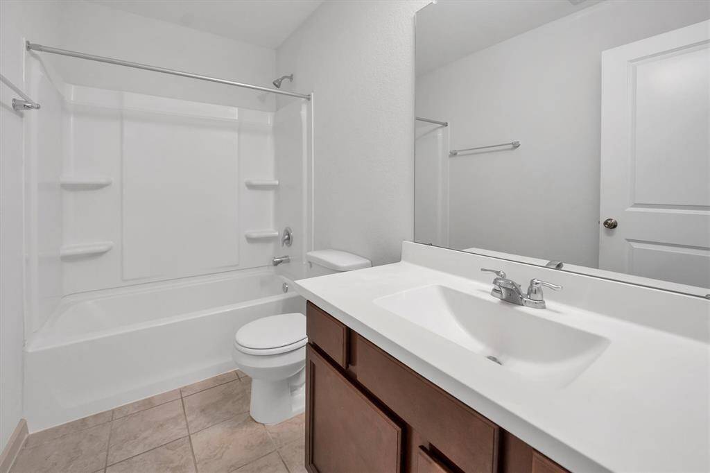 This secondary bathroom features a clean, modern design with a white tub-shower combo, a spacious vanity with a large mirror, and neutral tile flooring.
