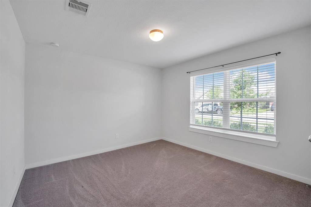 This secondary bedroom features neutral walls, carpeted flooring, and a large window offering ample natural light and a view of the outside. It's a versatile space ready to be customized to your needs.