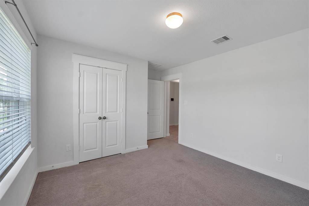This room features neutral walls, a large window with blinds for natural light, carpeted flooring, and a double-door closet, providing a clean and bright space.