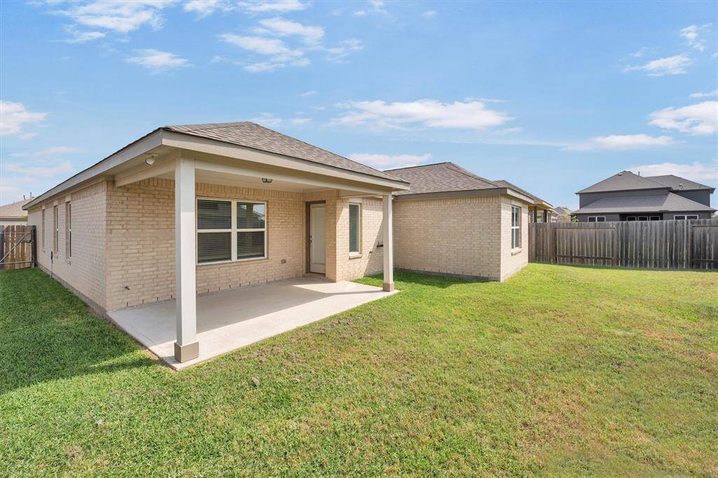 This photo showcases the backyard of a home featuring a covered patio and a spacious lawn. The exterior is brick, and the yard is enclosed by a wooden fence, providing privacy and space for outdoor activities.