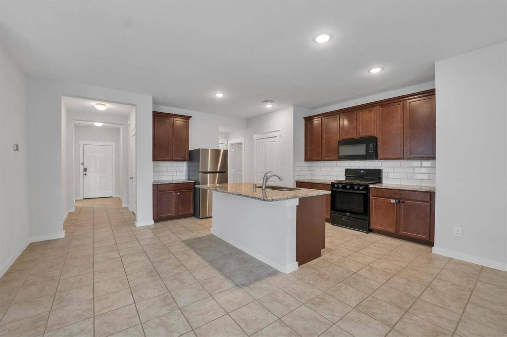 This spacious kitchen features modern stainless steel appliances, dark wood cabinetry, and a granite island. The open floor plan extends into a tiled dining area, providing a bright and functional space perfect for entertaining.