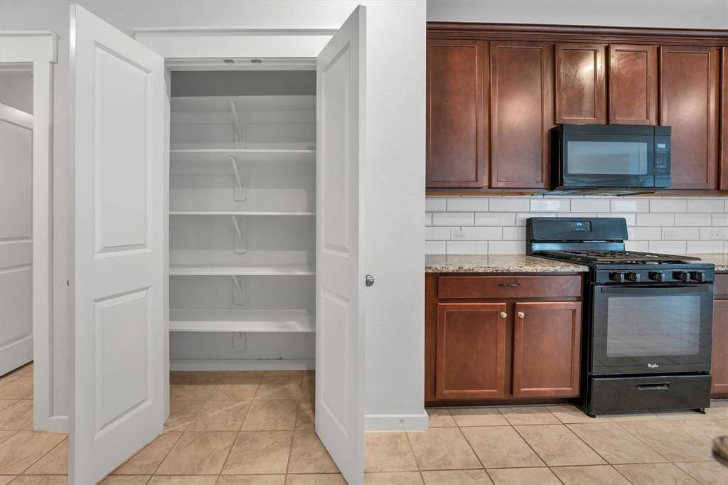 Discover a spacious kitchen with modern tile flooring, granite countertops, and ample cabinetry. Enjoy black appliances, a large island with a sink, and a stylish gas range for ultimate functionality.