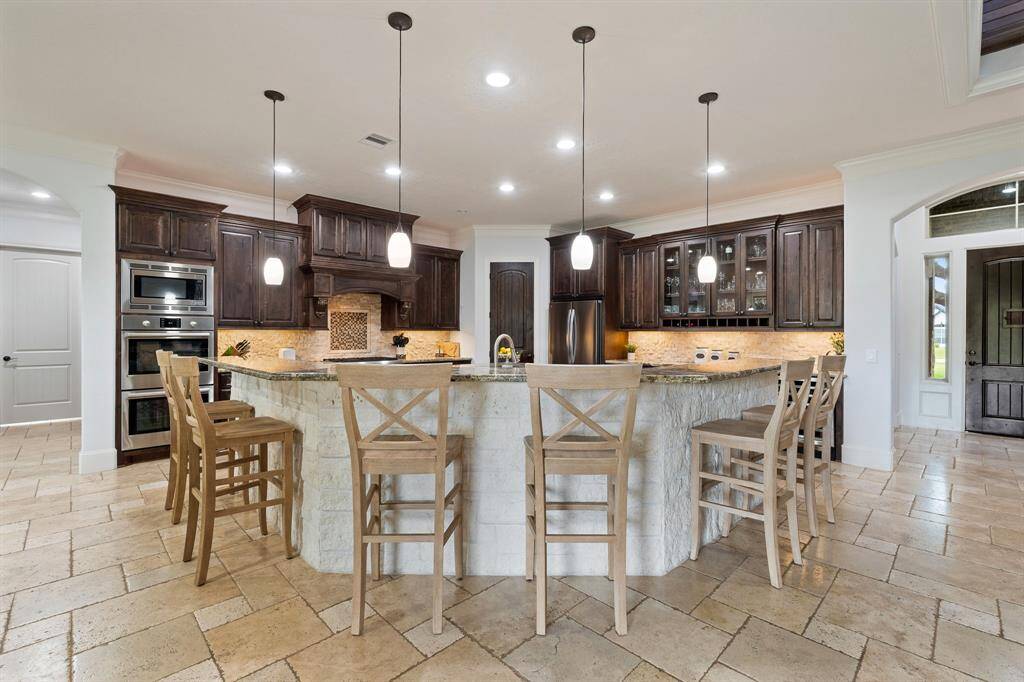 An abundance of additional seating can be found at this bar-height, wrap-around, countertop. The clean white stone façade mimics the backsplash just beyond. Pull up a chair and await the delicious feast the home chef is preparing.