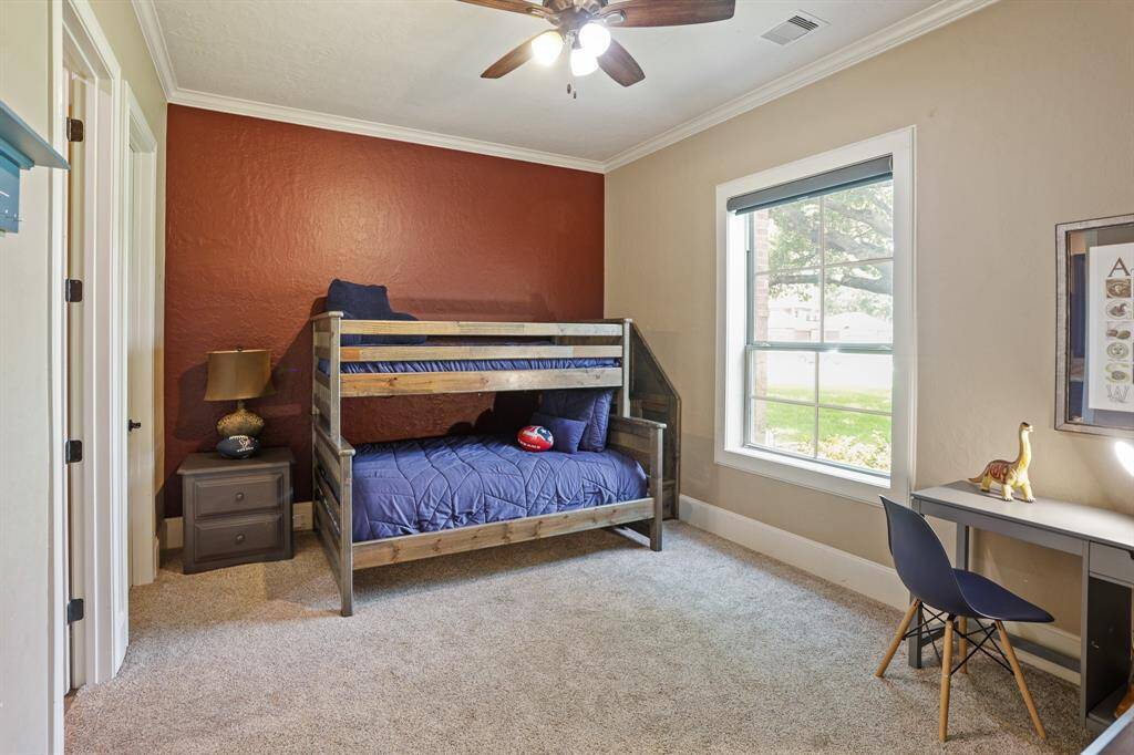 This Secondary Bedroom comes equipped with crown molding, plush carpeting, an accent wall, large walk-in closet, and ensuite bathroom. The cased window overlooks the Front Yard and is shaded by the majestic oak tree.