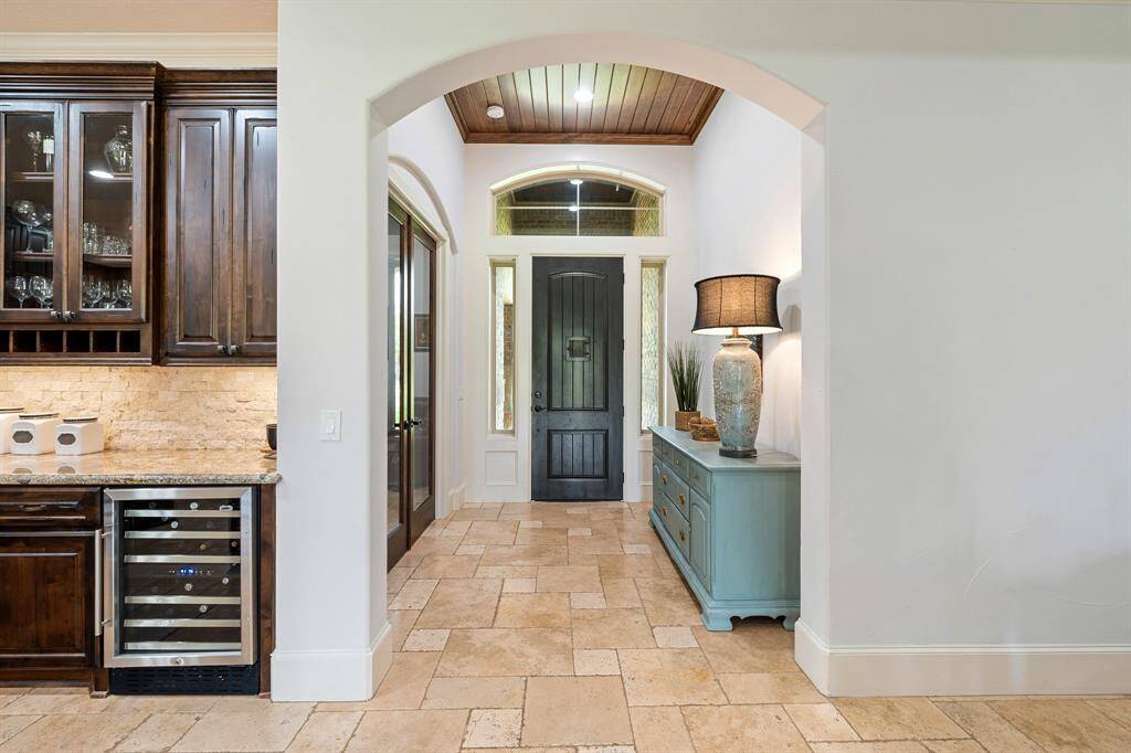 A look back at the grand front door showcases the abundance of natural light that fills the Foyer through the sidelights and transom above. The wood-paneled ceiling adds warmth and draws the eyes upward. The glass-paned double doors to the left lead to the home’s Study.