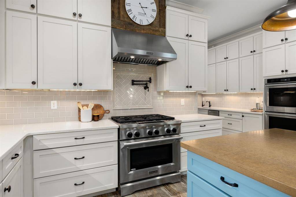 High end Kitchen Aid appliances include gas range with electric oven, stainless steel vent hood with solid stained wood accent, pot filler, double wall electric ovens, built-in microwave, and upper cabinets all the way around the kitchen.