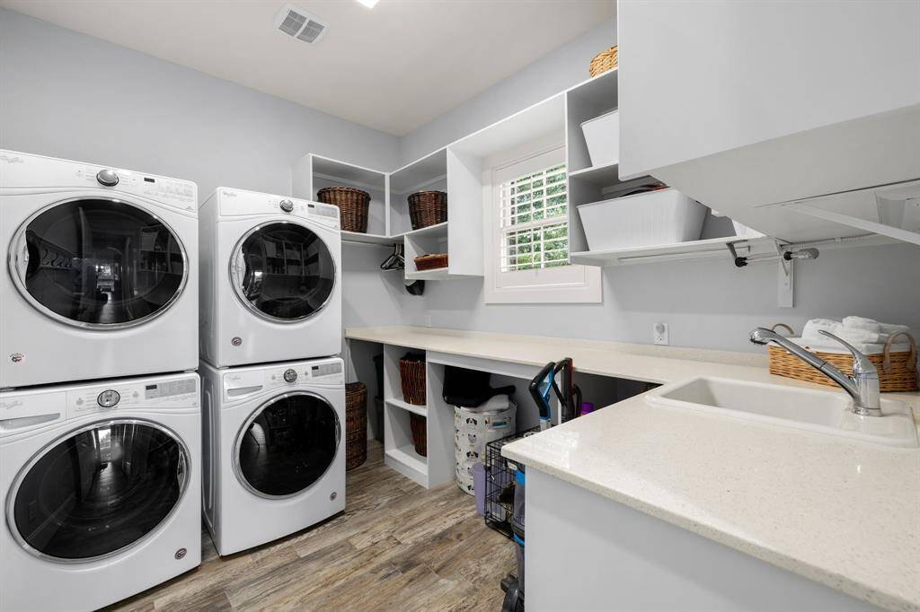 The laundry room is equipped with double washing machines and dryers, a sink, and is incredibly functional with cabinetry and shelving for storage.