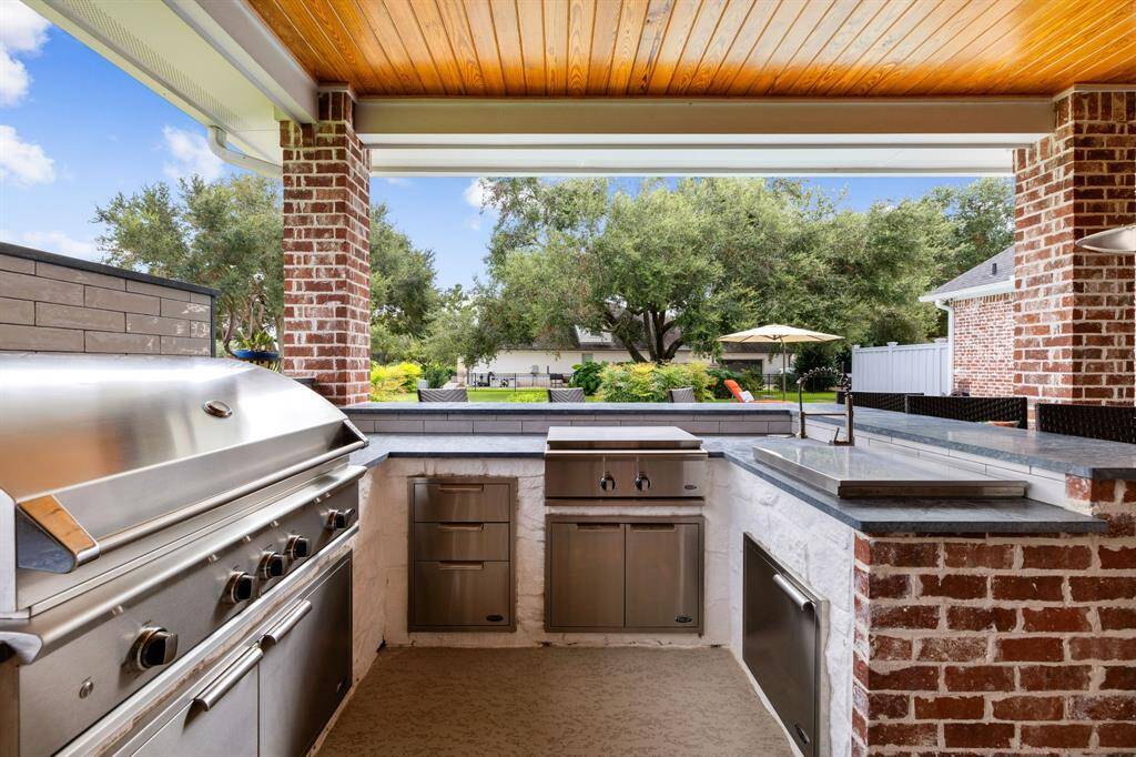 Outdoor kitchen with grille, gas burner, sink, storage drawers and cabinets, and bar seating.