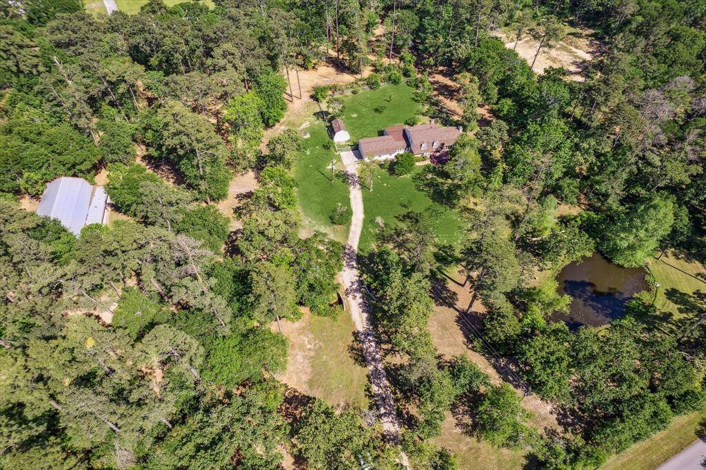 View of home and tree covered property with pond at the front of the property. Property line runs just left of the house and driveway and doesn't include the metal building on the left.