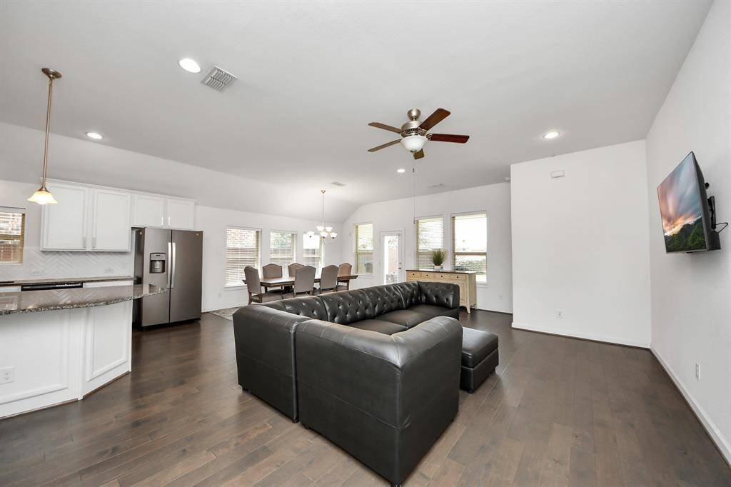 This spacious open-concept living area features comfortable seating area with a mounted TV. The room is brightened by ample natural light and modern lighting fixtures, offering a welcoming and functional space for entertaining and relaxation.