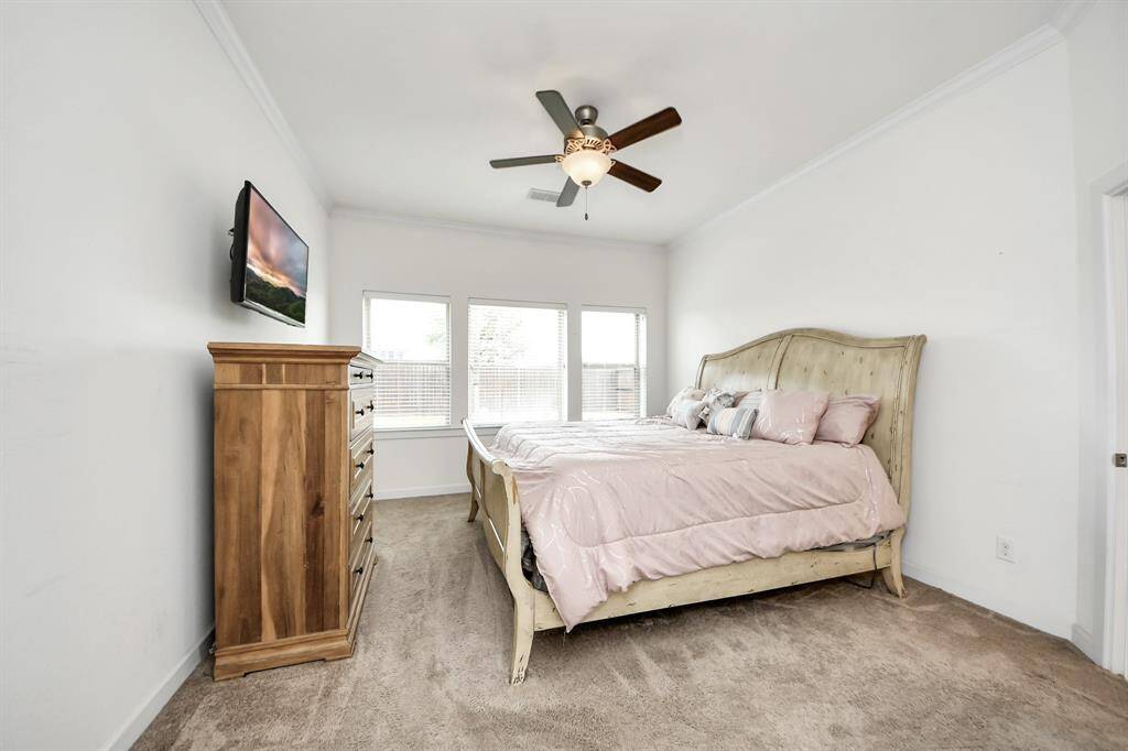 Spacious primary bedroom featuring abundant natural light, plush carpeting, and a stylish ceiling fan for added comfort.
