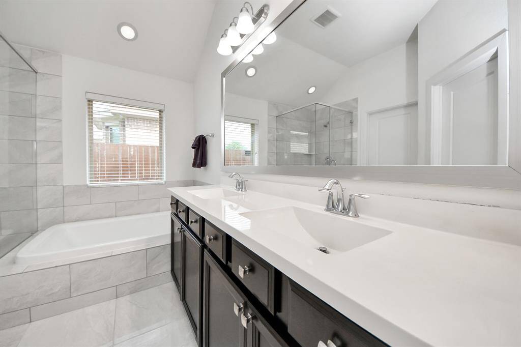 Experience luxury in the primary bath with a sleek double vanity, spacious glass walk-in shower, and inviting soaking tub, all enhanced by elegant fixtures and abundant natural light.