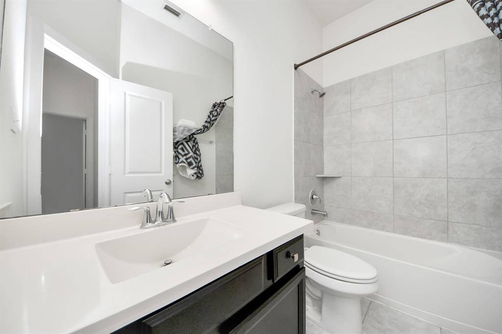 This stylish secondary bathroom features a sleek vanity, modern fixtures, and a tiled shower-tub combo, perfect for guests or family.