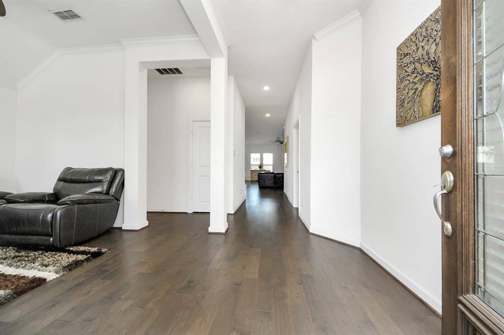 This inviting living area features a stylish wooden front door with decorative glass, modern leather seating, and a ceiling fan. The room is brightened by large windows, and a striped rug adds warmth to the hardwood floors.