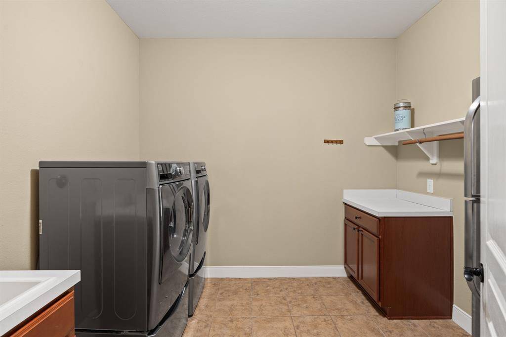 This spacious laundry room offers plenty of counter space, a handy sink, and room for an extra refrigerator, making laundry day a breeze while keeping everything organized and accessible.