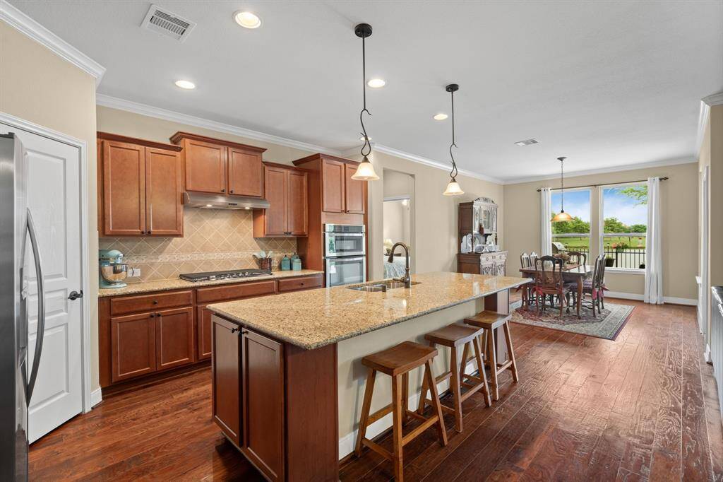 The kitchen shines with an oversized island, rich warm cabinetry, sleek built-in appliances, and wood flooring that adds warmth and continuity throughout the space.