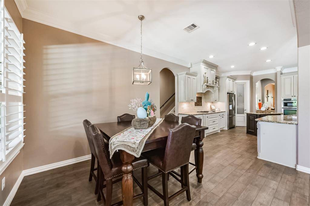 This photo showcases an elegant kitchen and dining area featuring  modern cabinetry, granite countertops, and a cozy dining space with a stylish chandelier. Natural light pours in through plantation shutters, creating a warm and inviting atmosphere.
