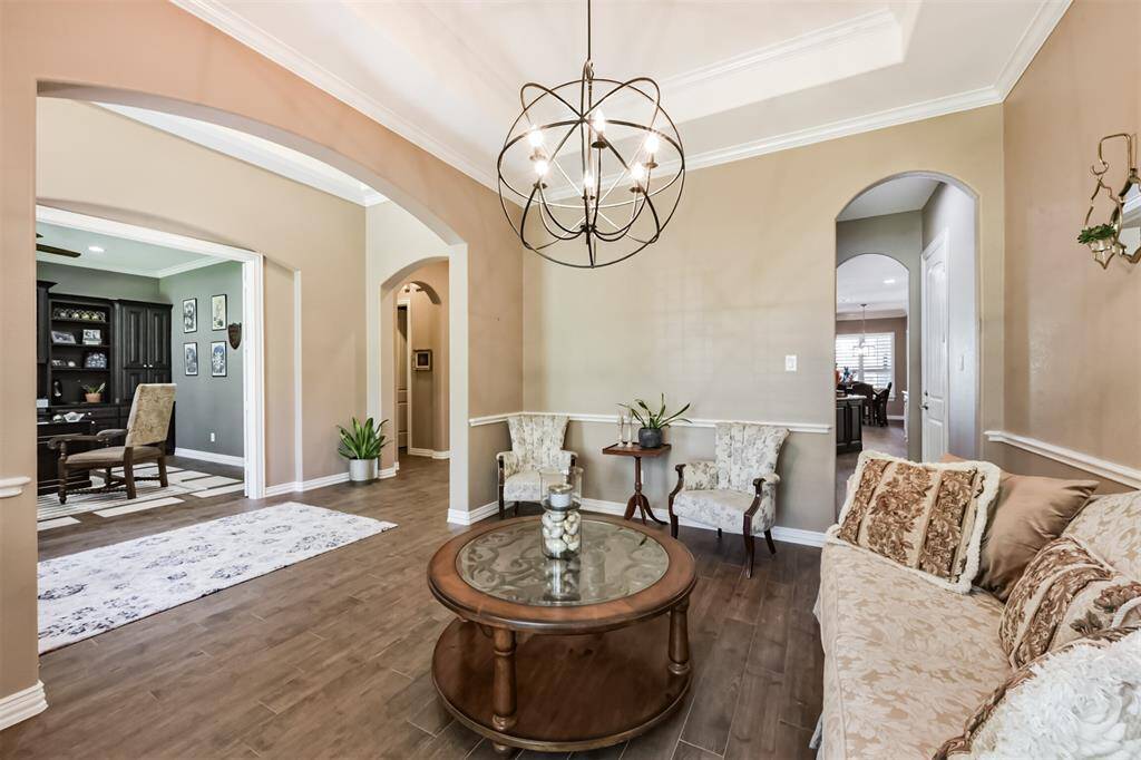 This photo showcases a spacious living area with elegant archways, wood tile flooring, and a stylish chandelier. The room is tastefully decorated with classic furniture as a formal sitting room, it offers a view into a study and dining area, creating an inviting and open feel.