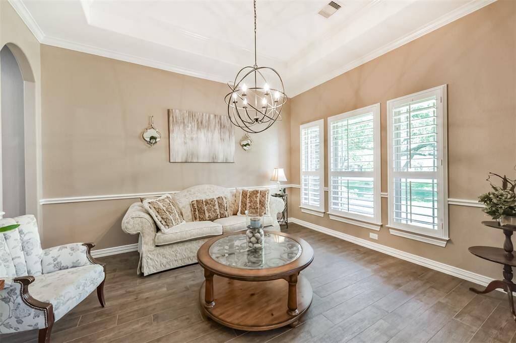This inviting living room features soft beige walls, elegant crown molding, and a stylish chandelier could also serve as a formal Dining Room. The Large windows with plantation shutters offer abundant natural light.