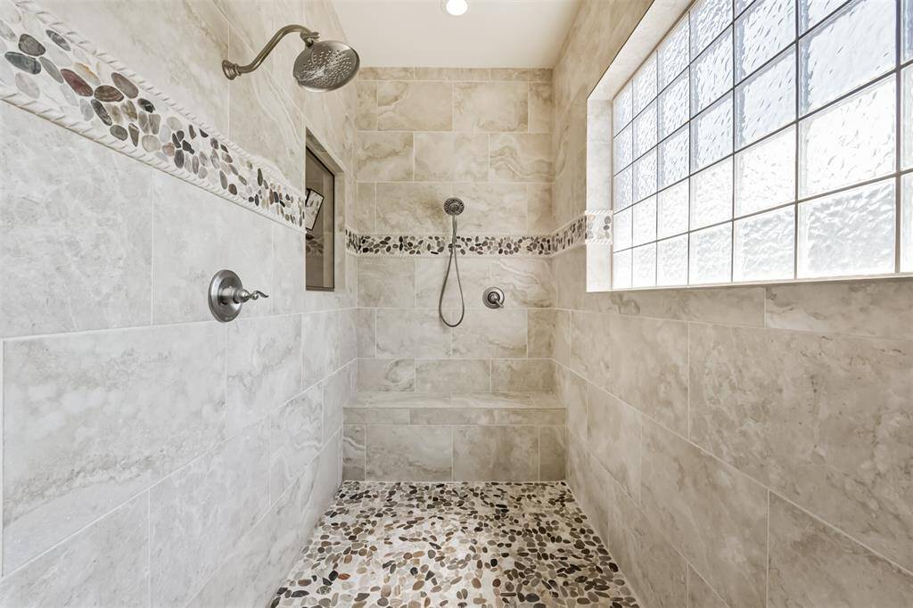 This spacious shower features elegant stone tile flooring, a built-in bench, and a glass block window for natural light. Decorative stone accents add a touch of luxury.