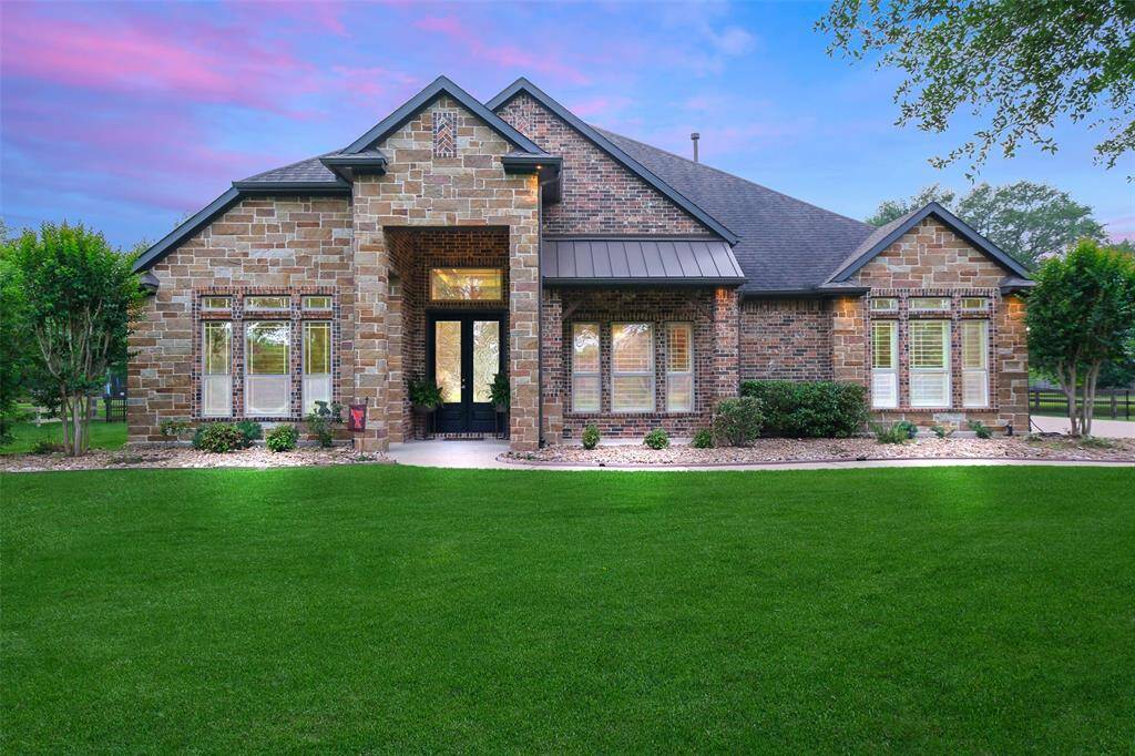 This beautiful home features a charming brick and stone exterior with large windows and a manicured front lawn. The inviting entrance is framed by elegant landscaping, and the roofline adds architectural interest to the facade.