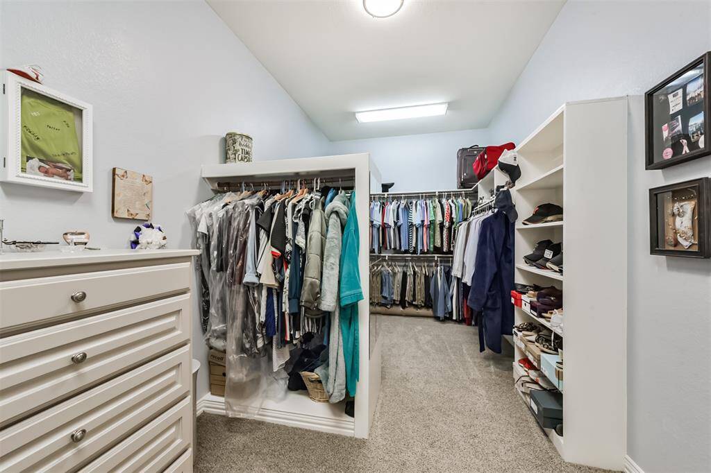 Spacious walk-in closet with ample storage, featuring hanging rods, open shelves, and a dresser. Well-lit with carpeted flooring, perfect for organizing clothing and accessories.
