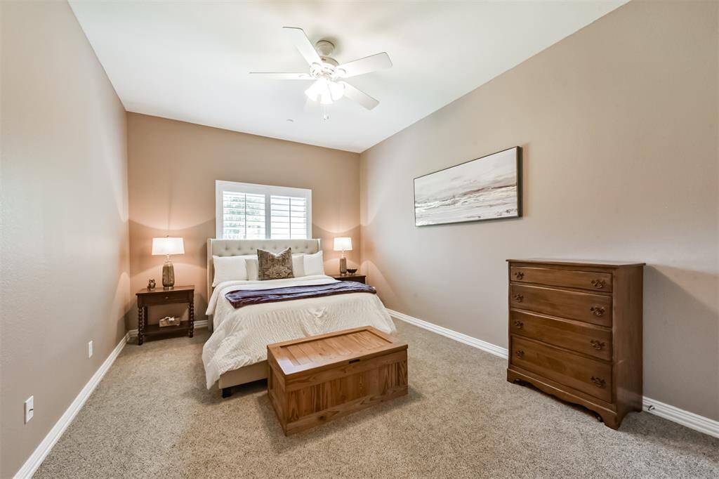 This cozy bedroom features neutral walls, carpeted flooring, and a ceiling fan and a window with plantation shutters, providing a bright and welcoming atmosphere.