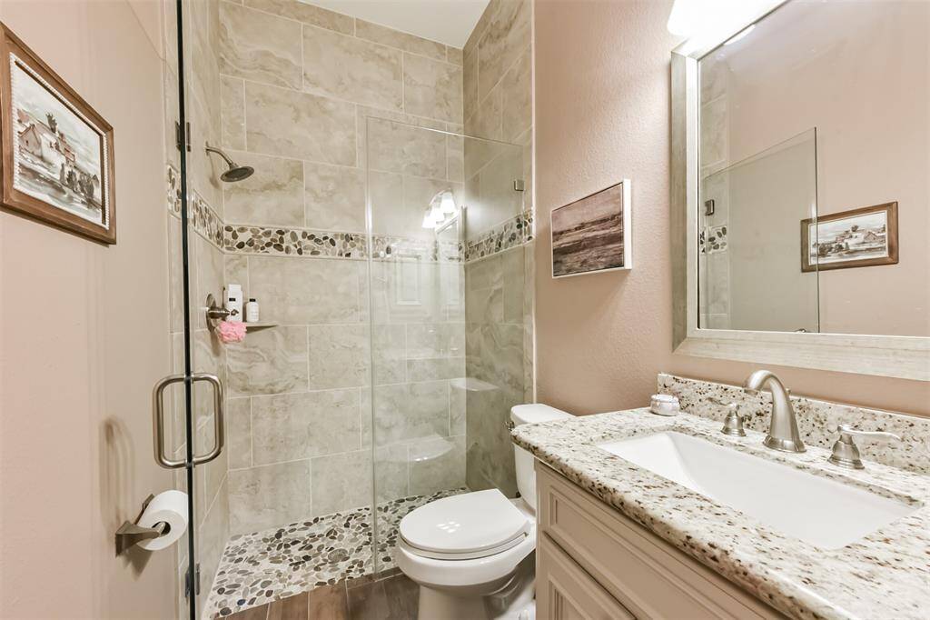 This bathroom features a modern design with a glass-enclosed shower boasting stone and tile accents. It includes a sleek, granite countertop with a stylish faucet and a large mirror. Neutral wall tones enhance the space.