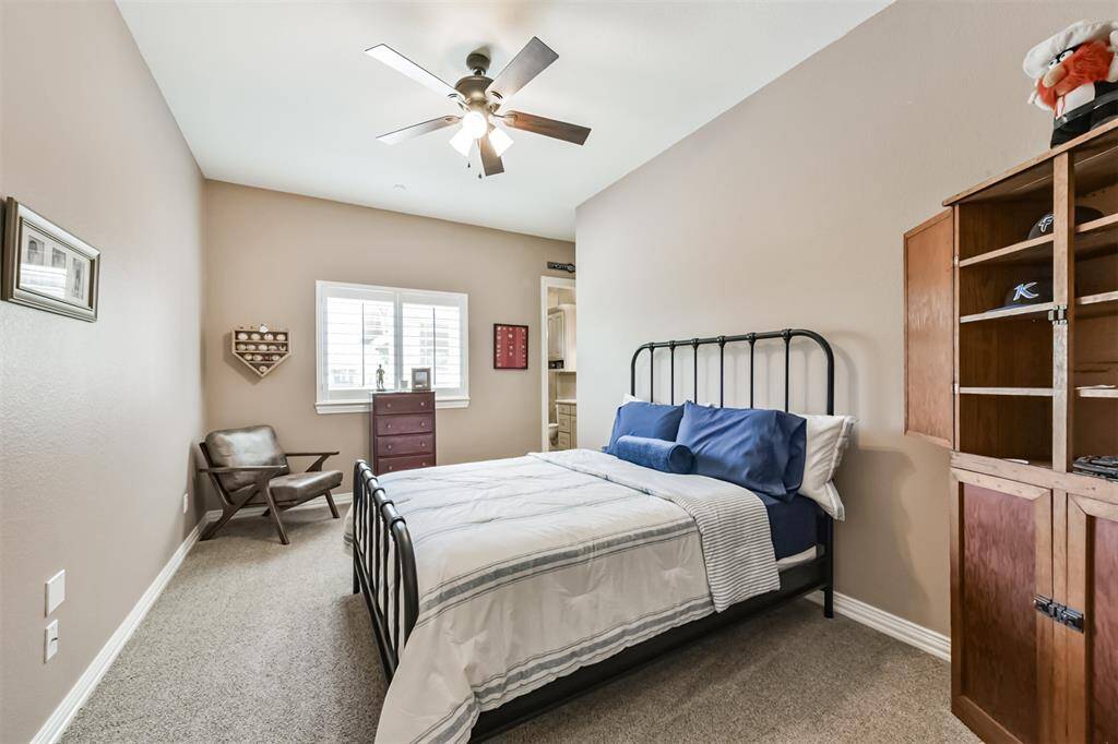 Cozy bedroom with neutral walls, carpeted flooring, and a ceiling fan. Natural light enters through a window, enhancing the room's warm ambiance.