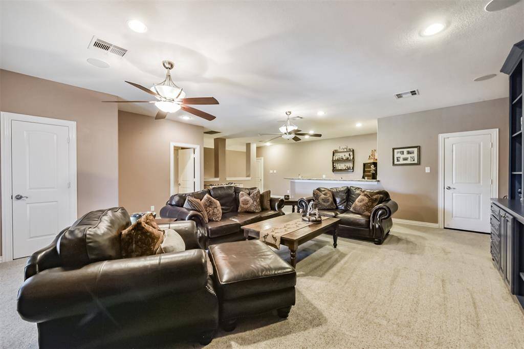 This spacious living area features, neutral walls, and carpeted floors. It includes two ceiling fans, recessed lighting, and a cozy atmosphere. The room connects to adjacent spaces, perfect for entertaining or family gatherings.