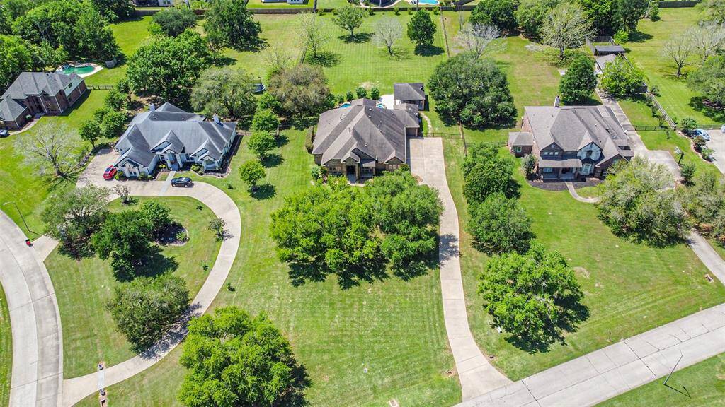 This aerial photo showcases a suburban neighborhood with three large, elegant homes, each featuring spacious yards and long driveways. The area is lush with greenery and mature trees, offering a serene and inviting environment.