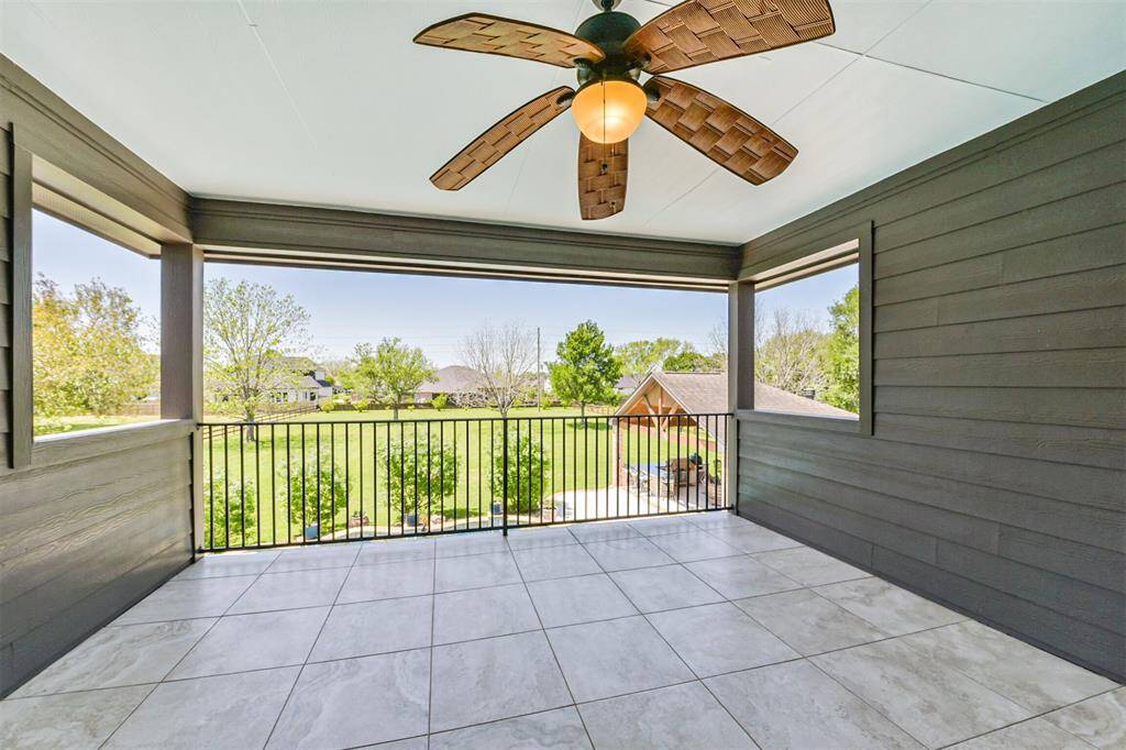 Spacious covered patio with tiled flooring, a ceiling fan, and a scenic view of the backyard, perfect for relaxing and entertaining.