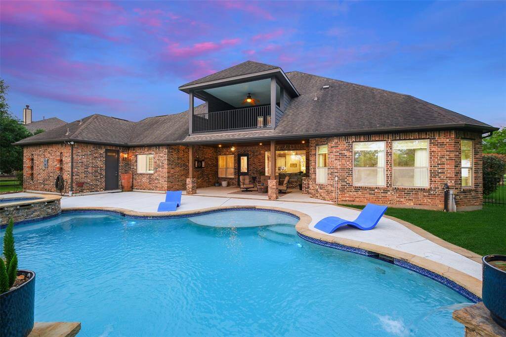 Dreamy, spacious backyard with a beautiful pool, hot tub, and patio area. The brick exterior complements the stylish design, and the covered balcony adds a charming touch. Ideal for entertaining and relaxation.