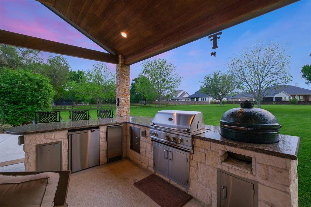 This outdoor kitchen features a covered patio with a built-in grill, smoker, and ample counter space. It overlooks a spacious, well-maintained backyard, perfect for entertaining.