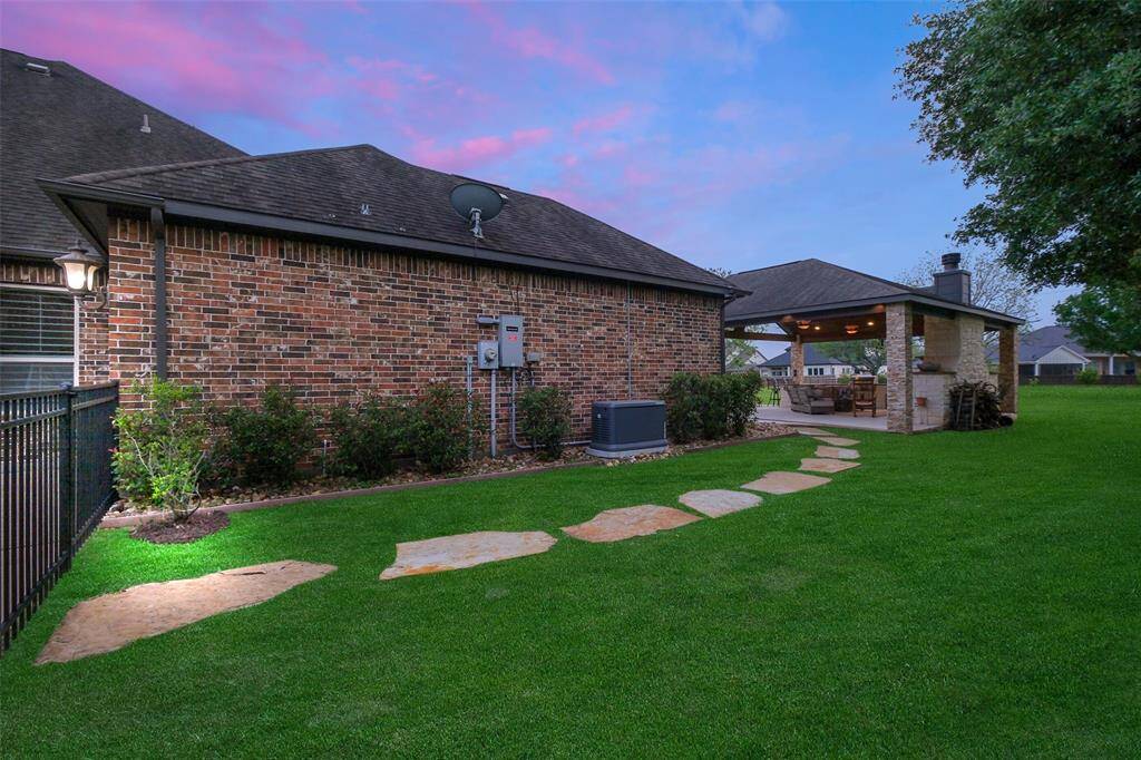 This photo features a charming backyard with a brick exterior, a well-maintained lawn, and a stone pathway leading to a cozy covered patio with a fireplace—ideal for outdoor entertaining.