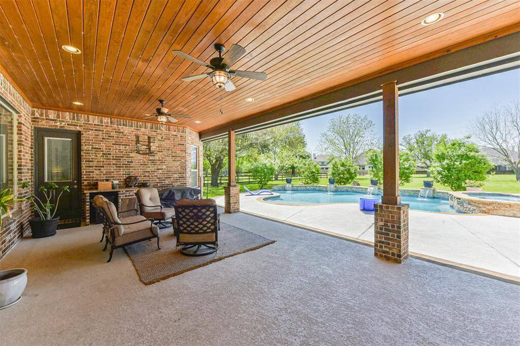 This inviting outdoor space features a covered patio with a wooden ceiling, ceiling fans, and comfortable seating attached to the home right outside the back door.
