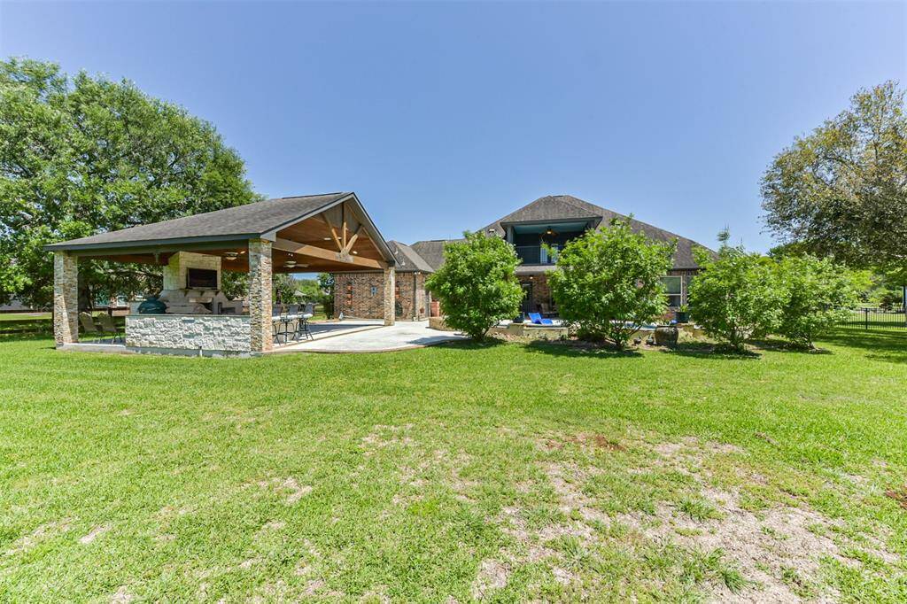 Spacious backyard with lush lawn, featuring a large covered patio area ideal for outdoor entertaining, and a charming brick house with a second-story balcony.