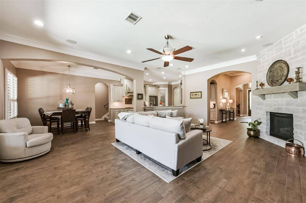 This spacious, open-concept living area features elegant floors, a cozy stone fireplace, and ample natural light. The room seamlessly connects to a dining area and a modern kitchen with a breakfast bar, creating a perfect space for entertaining.