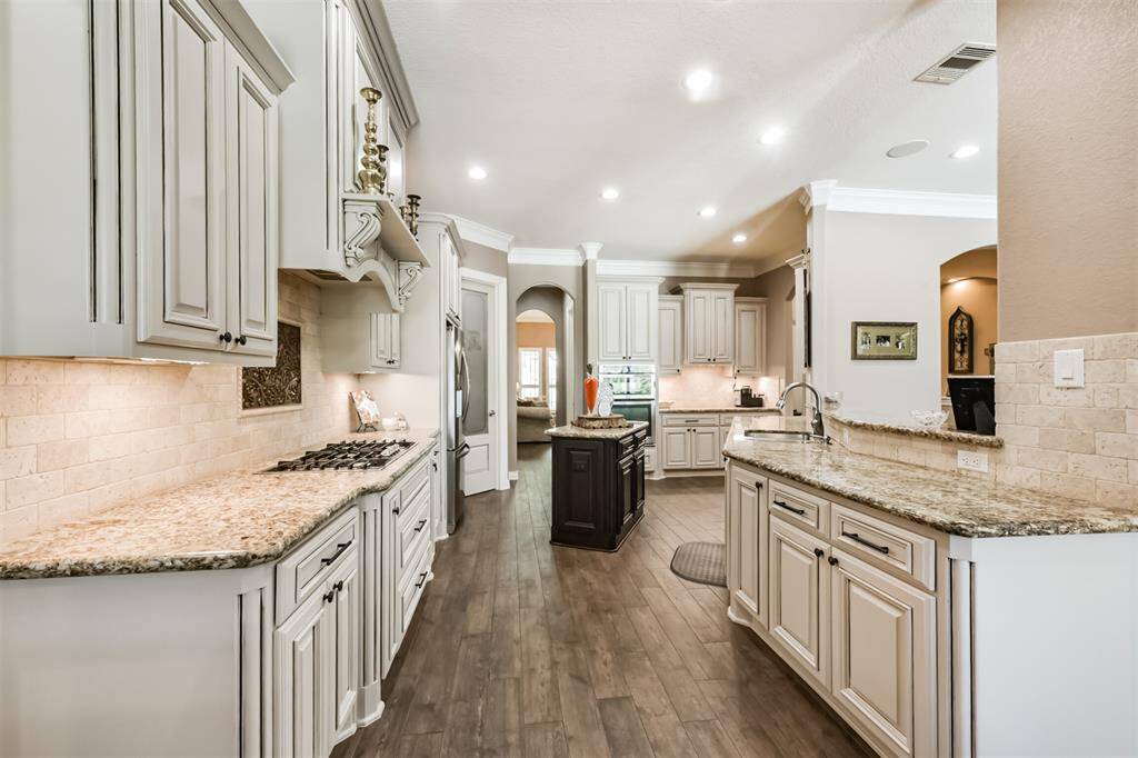 This spacious kitchen features elegant cabinetry, granite countertops, and a central island. It boasts modern appliances, ample storage, and recessed lighting, creating a bright and inviting space perfect for cooking and entertaining.