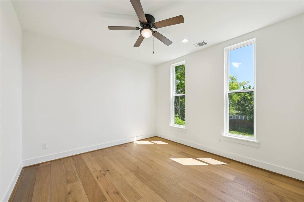 This bright, airy room features large windows, light hardwood floors, and a ceiling fan, creating a welcoming and comfortable space.