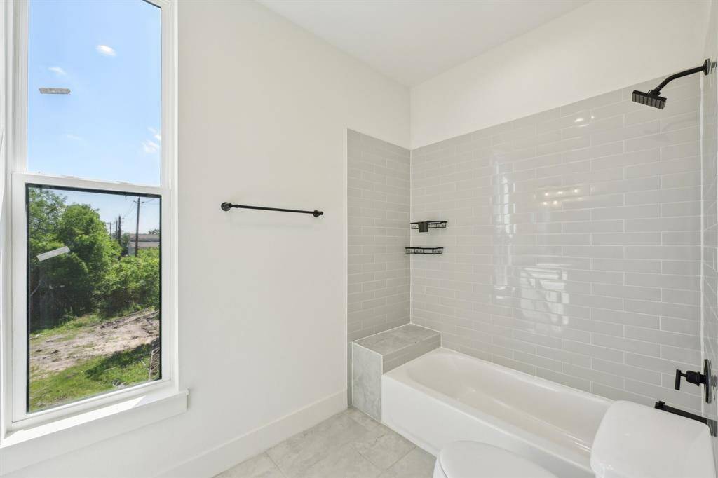 Bright and modern bathroom featuring a large window with natural light, a stylish bathtub with sleek gray subway tiles, and matte black fixtures.