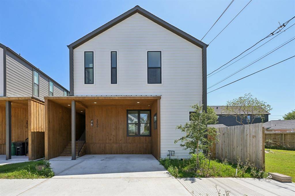 Modern two-story home with a minimalist design. Features a mix of wood and white paneling, large vertical windows, and a covered carport.