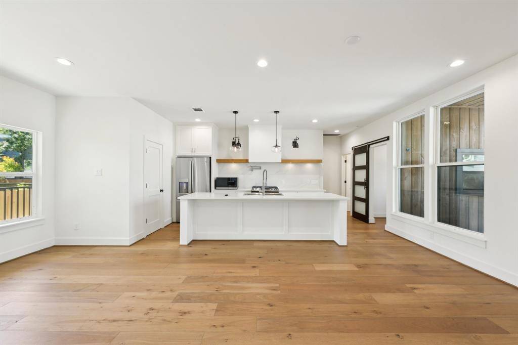 Bright and spacious kitchen with modern design, featuring a large island, stainless steel appliances, and wooden flooring. Abundant natural light from large windows adds to the inviting atmosphere.