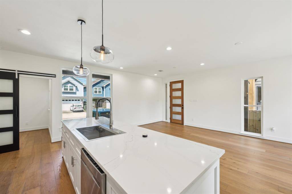 Bright, open-concept kitchen and living area with modern fixtures, hardwood floors, and a sleek island.