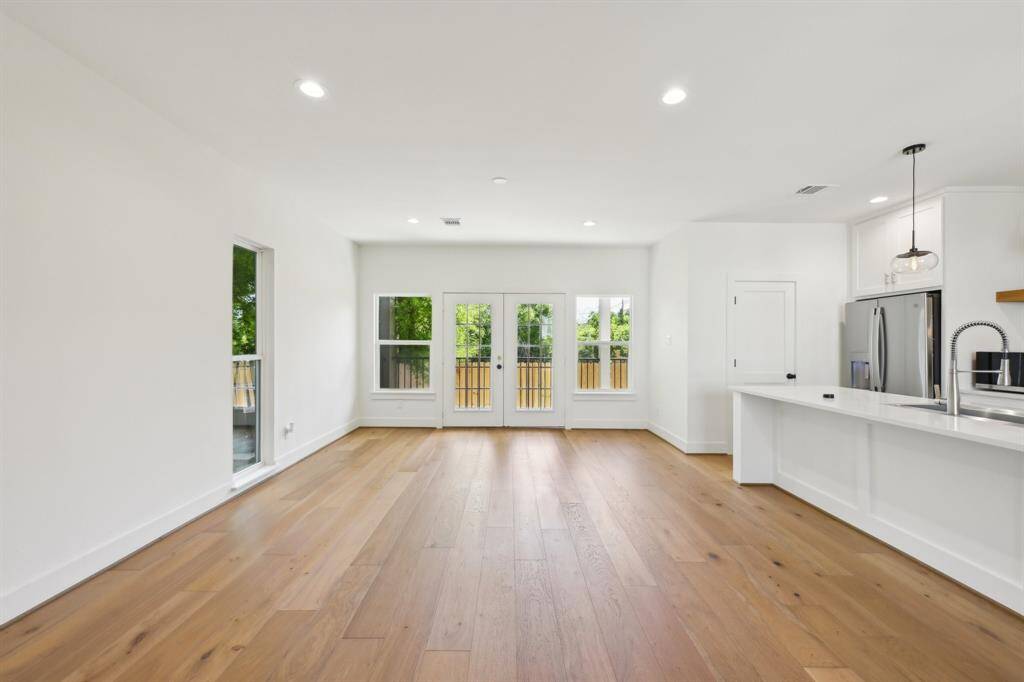 Bright and spacious open-plan living area with hardwood floors, large windows, and a modern kitchen featuring stainless steel appliances and a peninsula counter.