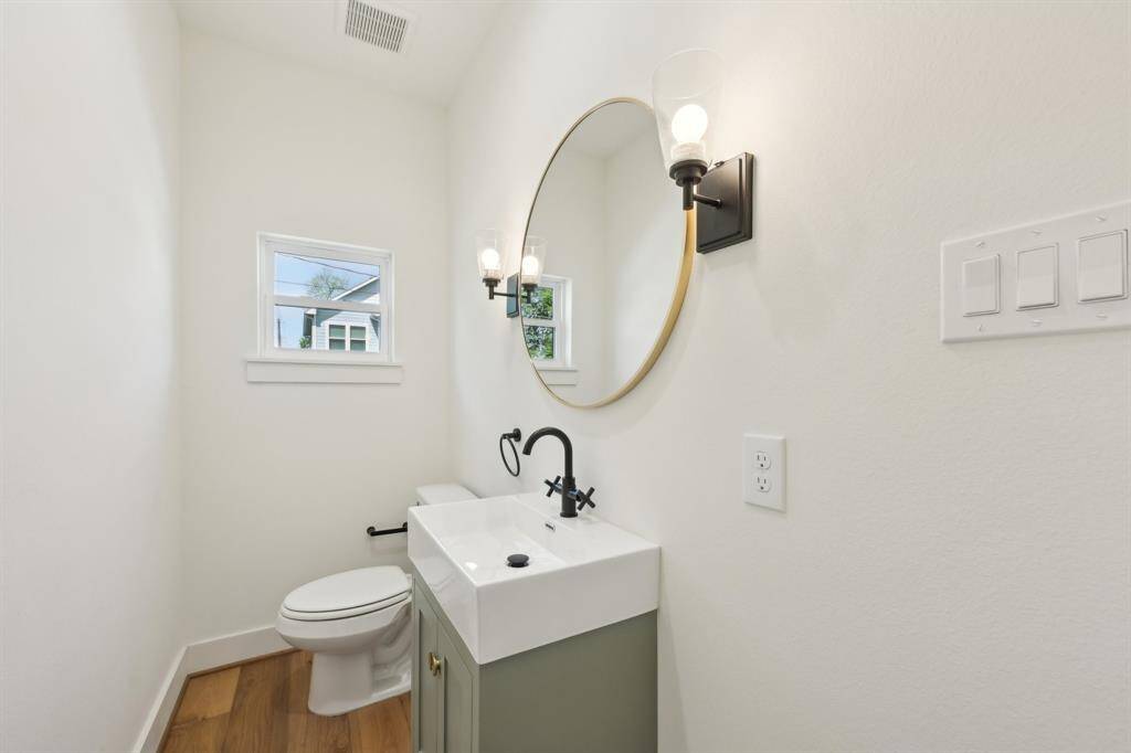 This is a modern, compact bathroom featuring a round mirror, single sink vanity, toilet, and stylish light fixtures.