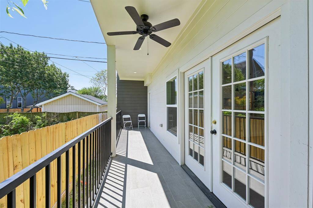 It has a covered front porch, large windows, and a driveway. The property is surrounded by a wooden fence with a spacious yard, offering privacy and a contemporary appeal.