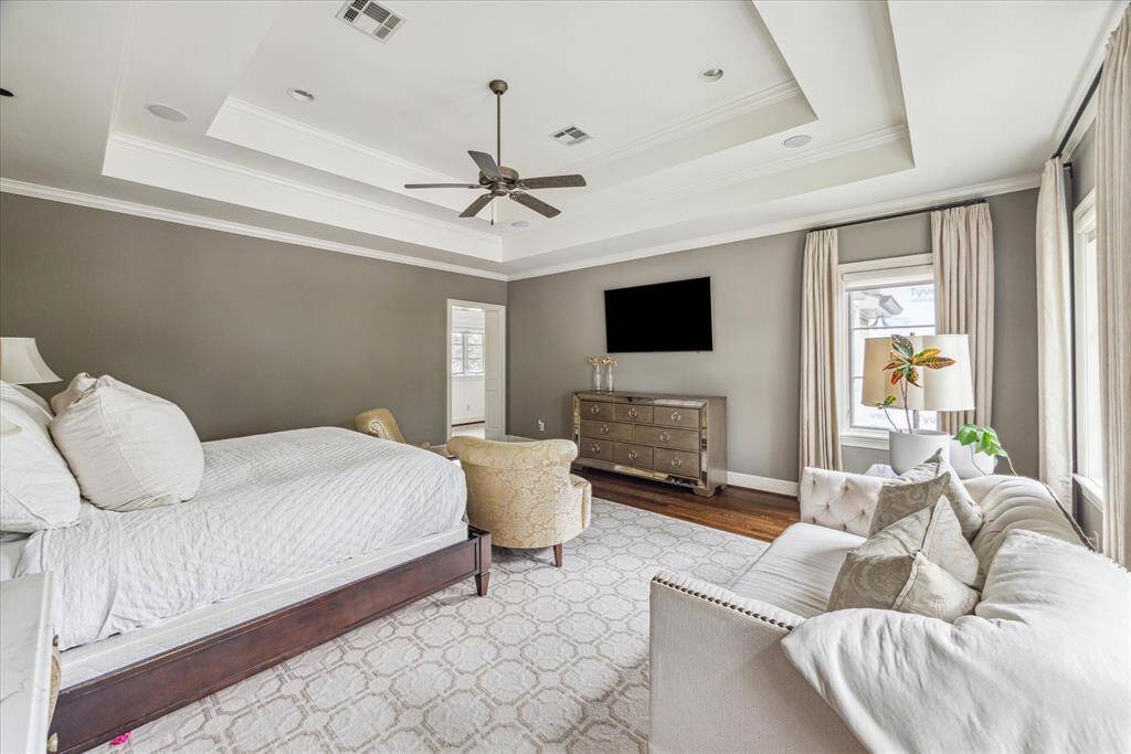 The spacious primary bedroom is a thoughtfully designed space with rich hardwood floors, a neutral palette, and elevated tray ceilings, combining comfort, style, and practicality for a true owner’s suite.
